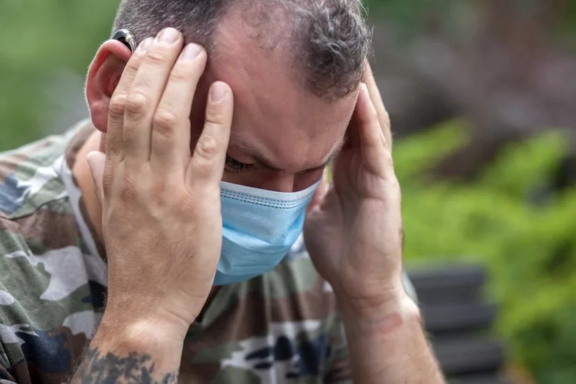 A 40-year-old man in a medical mask is in the park with his hands on his head due to a headache. Protection against coronavirus COVID-19 SARS-CoV-2 infection